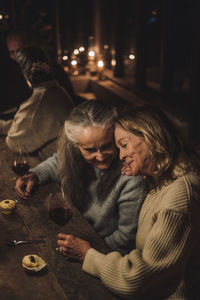 Smiling senior female friends with wineglasses sitting at dining table during party