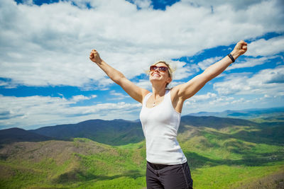 Happy young woman standing on mountain against sky