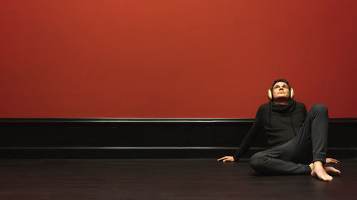 Portrait of young man sitting on red wall