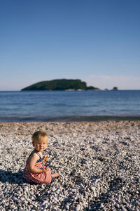 Boy sitting on rock at beach against sky