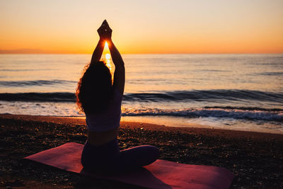 Rear view of woman standing at beach against sky during sunset