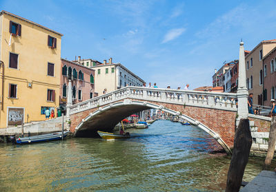 Bridge over canal by buildings against sky