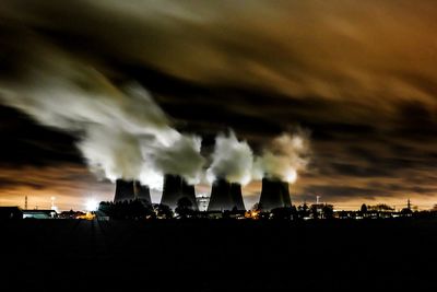 Illuminated smoke against cloudy sky at night