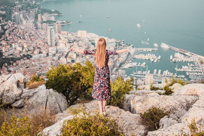 Young woman with long hair in dress on cliff. panoramic view of monaco, sea coast, french riviera.