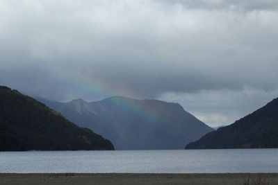 Scenic view of rainbow over sea and mountains against sky