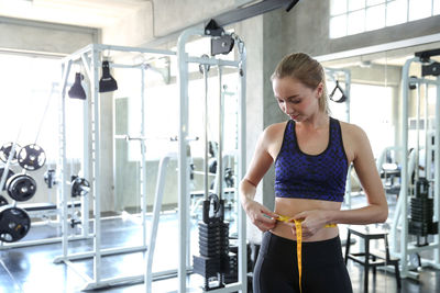 Young woman measuring waist in gym