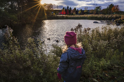 Toddler girl watching duck on a lake during fall sunset