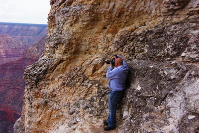 Side view of man photographing through camera while standing on mountain