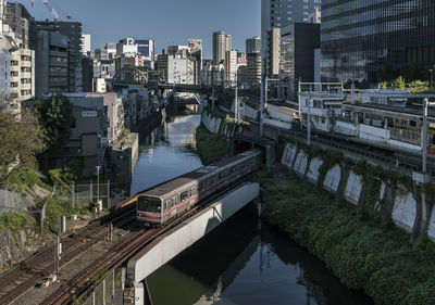 Train on bridge over river amidst buildings in city
