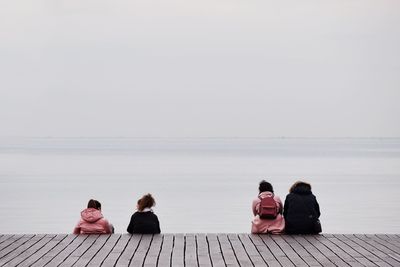 Rear view of people sitting on pier over sea against sky