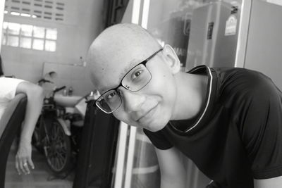 Portrait of smiling bald teenage boy wearing eyeglasses at home