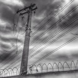 Low angle view of electricity pylon against cloudy sky