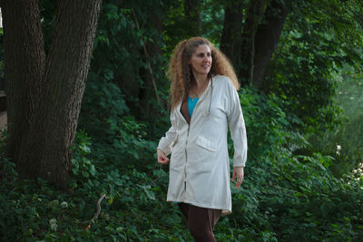 Smiling mature woman looking away while standing against trees