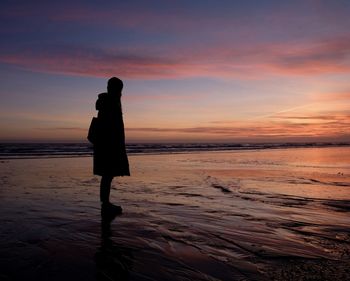Silhouette woman standing at beach against sky during sunset reflection