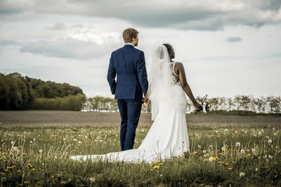 Rear view of friends standing on field against sky