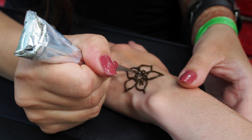 Cropped hand of artist applying henna tattoo on human hand