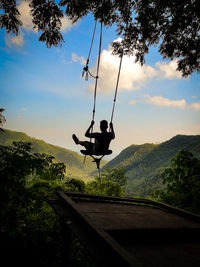 Rear view of man sitting on swing against sky