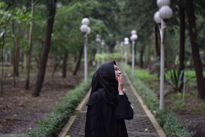 Smiling woman wearing hijab standing on footpath in park