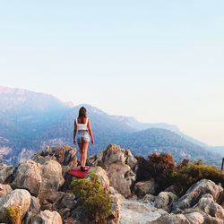 Side view of woman standing on rock against sky