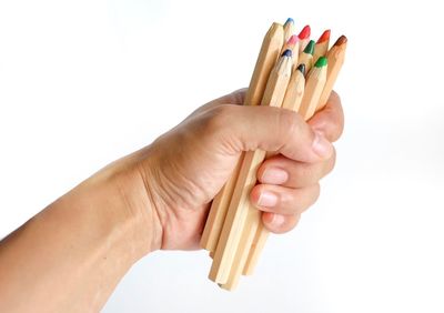 Close-up of hand holding pencils against white background