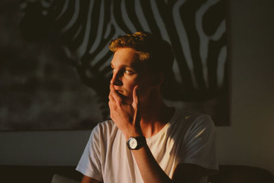 Portrait of young man sitting against wall at home