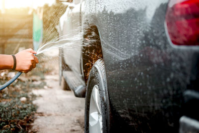 Cropped hand spraying water on car at field