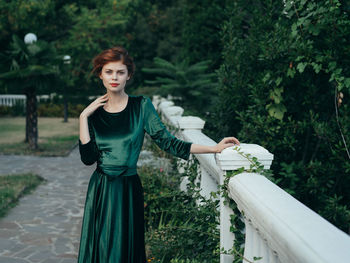 Portrait of young woman standing by railing outdoors