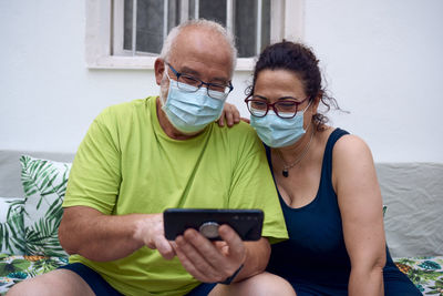 An elderly couple with surgical masks while using a mobile phone. elderly people