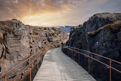 Tourists walking on bridge amidst rock formations at thingvellir national park