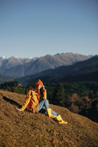 Rear view of woman sitting on mountain against sky