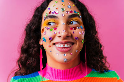 Close-up portrait of smiling young woman wearing mask against pink background