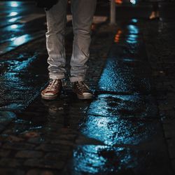 Low section of man standing by puddle on road at night