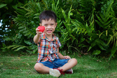 Portrait of boy holding heart shape on field