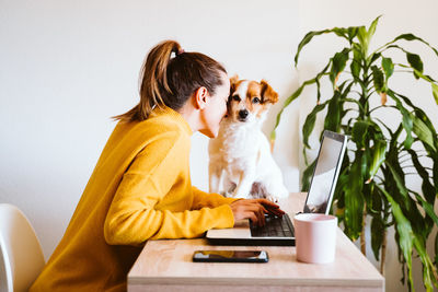 Side view of woman playing with dog while using laptop