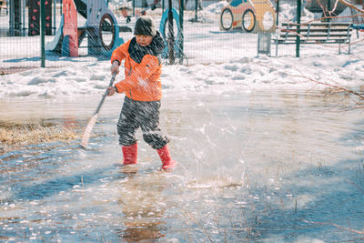 Small boy in vibrant winter gear disrupts quiet of thawing landscape, turning simpl on playground