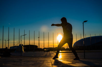 Low angle view of silhouette man standing on beach against clear sky during sunset