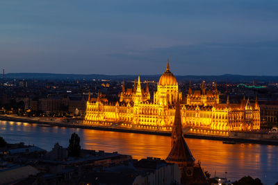 Illuminated city at waterfront against sky at dusk