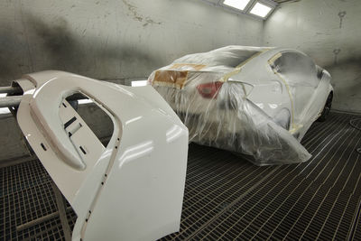 The photograph captures the scene of an automotive workshop the process of painting car parts.