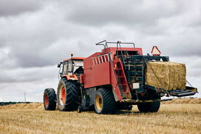 Dried hay roll and modern tractor placed on agricultural field in mountainous area in summer