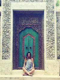 Full length portrait of woman sitting at entrance of building
