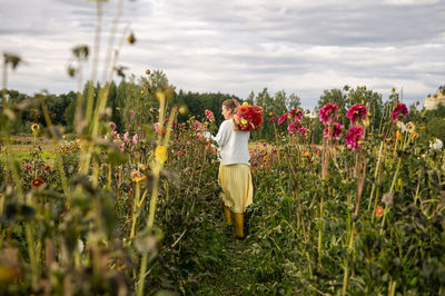 A girl in rubber boots collects autumn flowers on the field