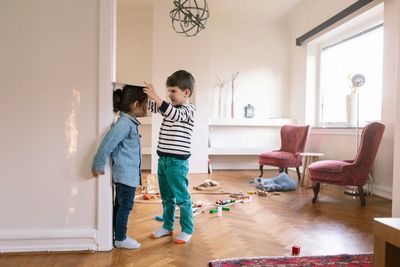 Brother measuring sister's height on wall with book at home