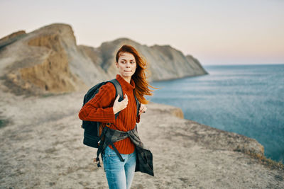 Portrait of smiling young woman standing on sea shore against sky