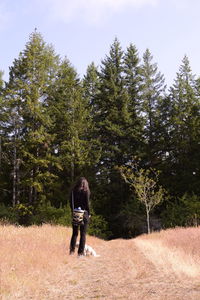 Rear view of man standing on field against trees in forest