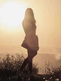 Woman standing on field against sky during sunset