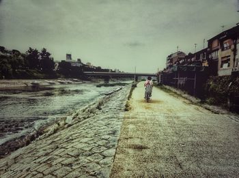 Man walking on street in city against sky