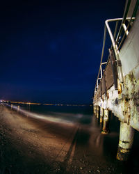 Illuminated beach by sea against sky at night