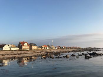 Buildings by sea against clear blue sky