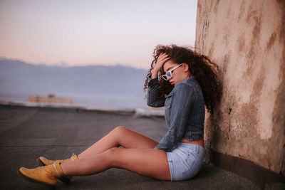 Side view of woman sitting against wall during sunset