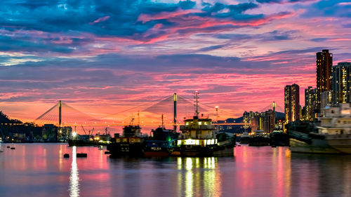 Illuminated harbor by river against sky during sunset